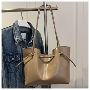 Dettaglio di una borsa tote beige lucida con spalline sottili e nodo decorativo raffinato