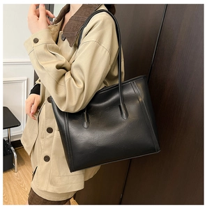 Detailed view of black leather tote bag worn by a model with elegant slim shoulder straps