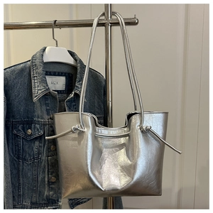 Dettaglio della borsa tote argento con texture stropicciata e nodo su denim