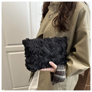 Detailed view of 3D rose fabric texture on a black evening clutch bag held by a model