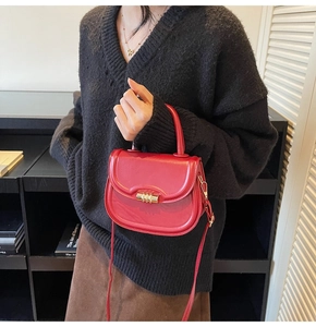 Detail of red leather saddle bag featuring a gold cylindrical lock and top handle strap
