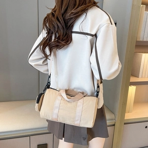 Back view of woman wearing a lightweight beige nylon cylinder bag with a round coin pouch