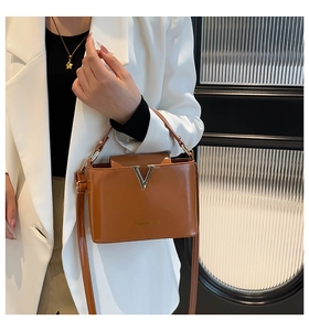 Detail of caramel glossy patent leather bucket bag with gold V-buckle on white blazer