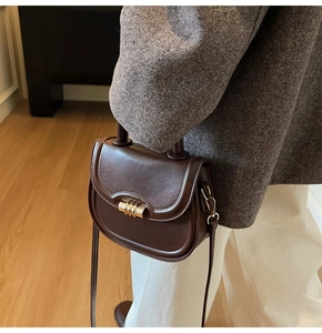 Detail of dark brown leather saddle bag with golden clasp worn with a grey wool blazer