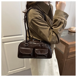 Dettaglio di una borsa a spalla marrone scuro lucida con due tasche frontali sul modello