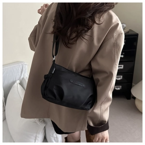 Detail of black crossbody tote bag featuring a branded logo plate and drawstring side pockets