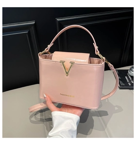 Close-up of pink leather bucket bag featuring a gold V-shaped buckle and top handle