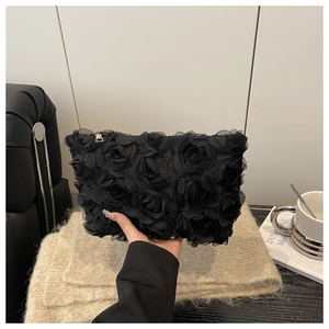 Close-up of black 3D rose textured clutch bag with gold zipper held by a hand