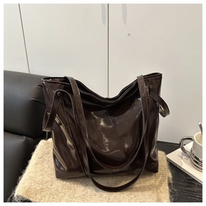 Detail of high-gloss chocolate tote bag on beige knit blanket in cozy home setting