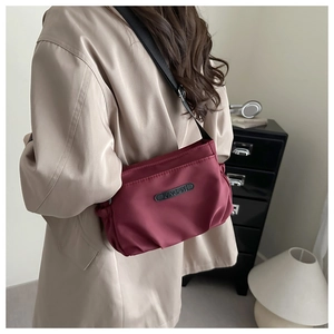 Macro detail of a burgundy nylon crossbody bag with adjustable wide black strap