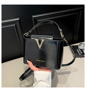 Close-up of black patent leather crossbody bag with gold V buckle and logo detail