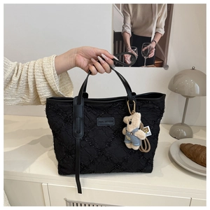 Détail du sac cabas matelassé noir avec texture gaufrée, logo et pendentif ourson bleu