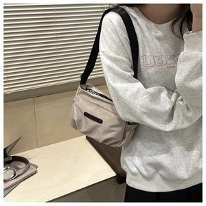 Detail of beige nylon tote bag with black adjustable strap worn as crossbody