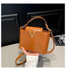 Detail of brown glossy leather bag with gold V-decoration and fashion logo imprint