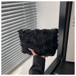 Detail of a black clutch bag featuring 3D chiffon rose floral texture and zipper closure
