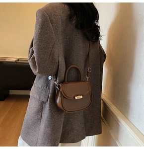 Brown semi-circle saddle bag with gold metal buckle shown on model in a minimalist room