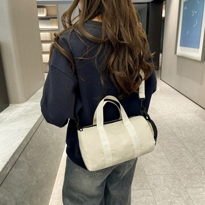 Modern nylon barrel bag worn by a model in a minimalist marble corridor setting