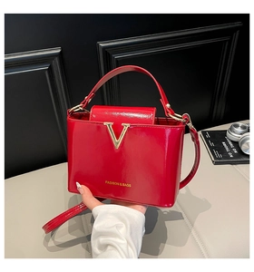 Close-up of bright red patent leather bucket bag featuring a gold V-shaped metal buckle
