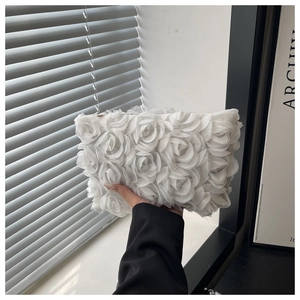 Detailed view of 3D fabric rose texture on a white clutch with gold zipper finish