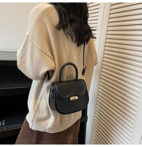 Model wearing a black leather saddle bag with gold buckle and top handle details