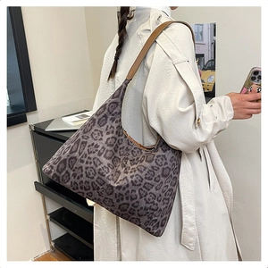 Detail of a large leopard print tote bag with brown leather strap on a model