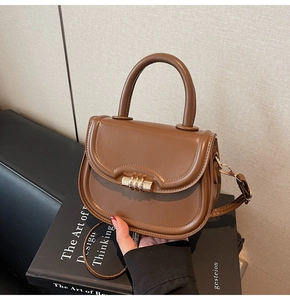 Close-up of brown vintage saddle bag with gold cylinder lock and detachable strap