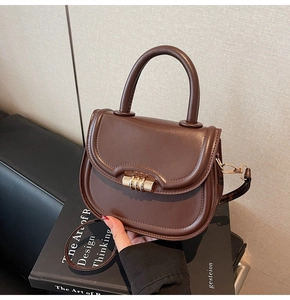 Detail of dark brown saddle bag with gold cylinder buckle on a design book background