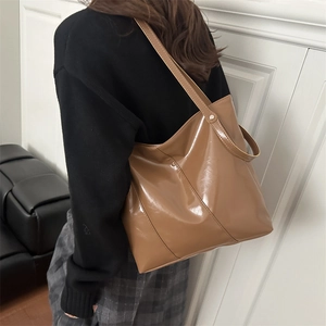 Chic caramel patent leather tote bag with glossy finish shown in a lifestyle shoulder view