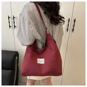 Detail of burgundy corduroy hobo bag with fashion logo tag and metal buckle strap