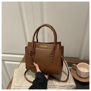 Détail d'un sac à main marron effet crocodile avec lettrage doré et anses