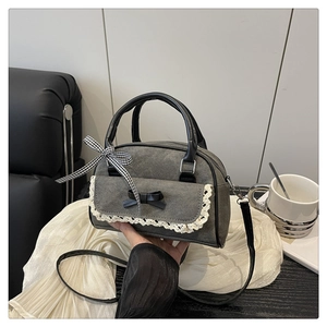 Détail du sac en tissu gris avec dentelle, nœud noir et ruban à carreaux sur un canapé