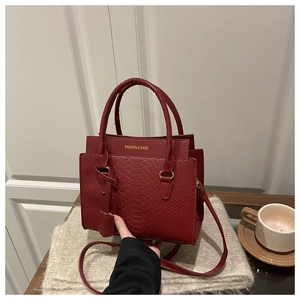 Détail du sac à main rouge foncé avec motif serpent et logo doré sur le devant