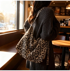 Detailed view of leopard print tote bag styled with a dark knit sweater in a cozy cafe