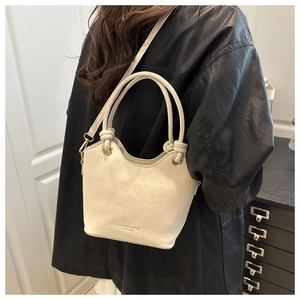 Detail of cream white leather bucket bag with wavy rim and knotted handle on model