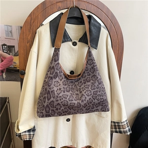 Retro leopard print velvet tote bag with brown leather straps hanging in a minimalist room