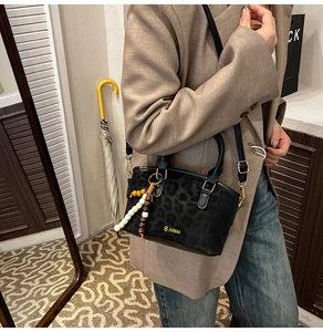Detail of black leopard print crossbody bag with wooden bead tassel and logo branding