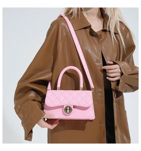 Bolso bandolera rosa acolchado con cierre dorado sobre abrigo de cuero marrón