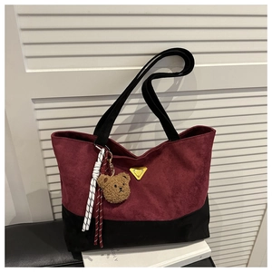 Detail of burgundy suede tote bag with yellow triangle logo and brown bear charm