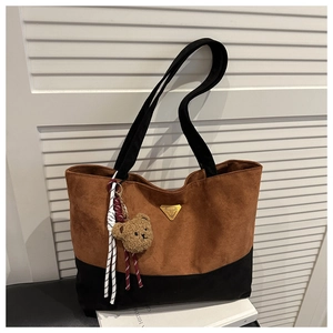 Detail of two-tone tote bag with brown suede, black fabric, and cute bear charm