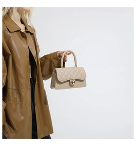 Detalle del bolso beige acolchado con cierre dorado circular y asa cilíndrica