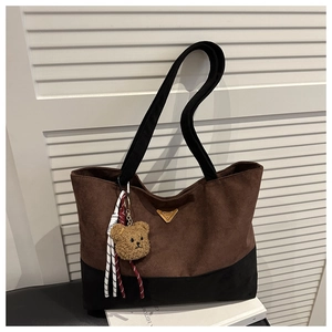 Close-up of two-tone tote bag with triangular metal plaque and cute bear charm accessory
