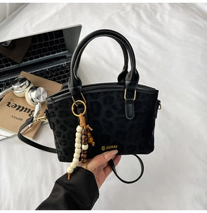 Dettaglio borsa nera con stampa leopardata, logo dorato e ciondolo di perline in legno