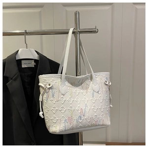 Detail of white quilted tote bag featuring colorful wavy embroidery and drawstring accents