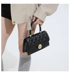 Detalle de bolso de mano en cuero acolchado negro con patrón de diamantes y cierre giratorio dorado