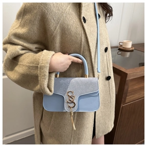 Detail of light blue crossbody bag with snakeskin texture and gold metal logo on model