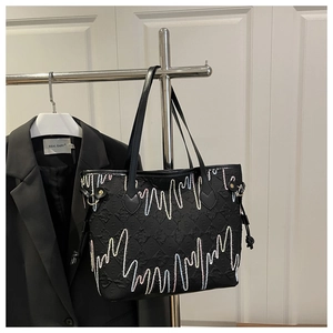 Close-up of black quilted tote bag featuring colorful wavy embroidery and side drawstrings