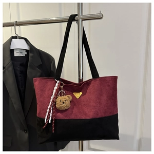 Detail of burgundy suede tote bag with golden triangle logo and cute bear charm