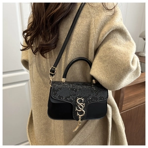 Detail of black snake pattern handbag with gold SS logo and tassel worn with coat
