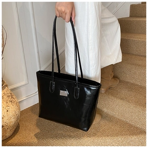Close-up of black glossy patent leather tote bag with silver metal plaque detail