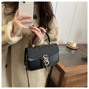 Detail of black crossbody bag featuring python-embossed flap and gold tassel metal buckle